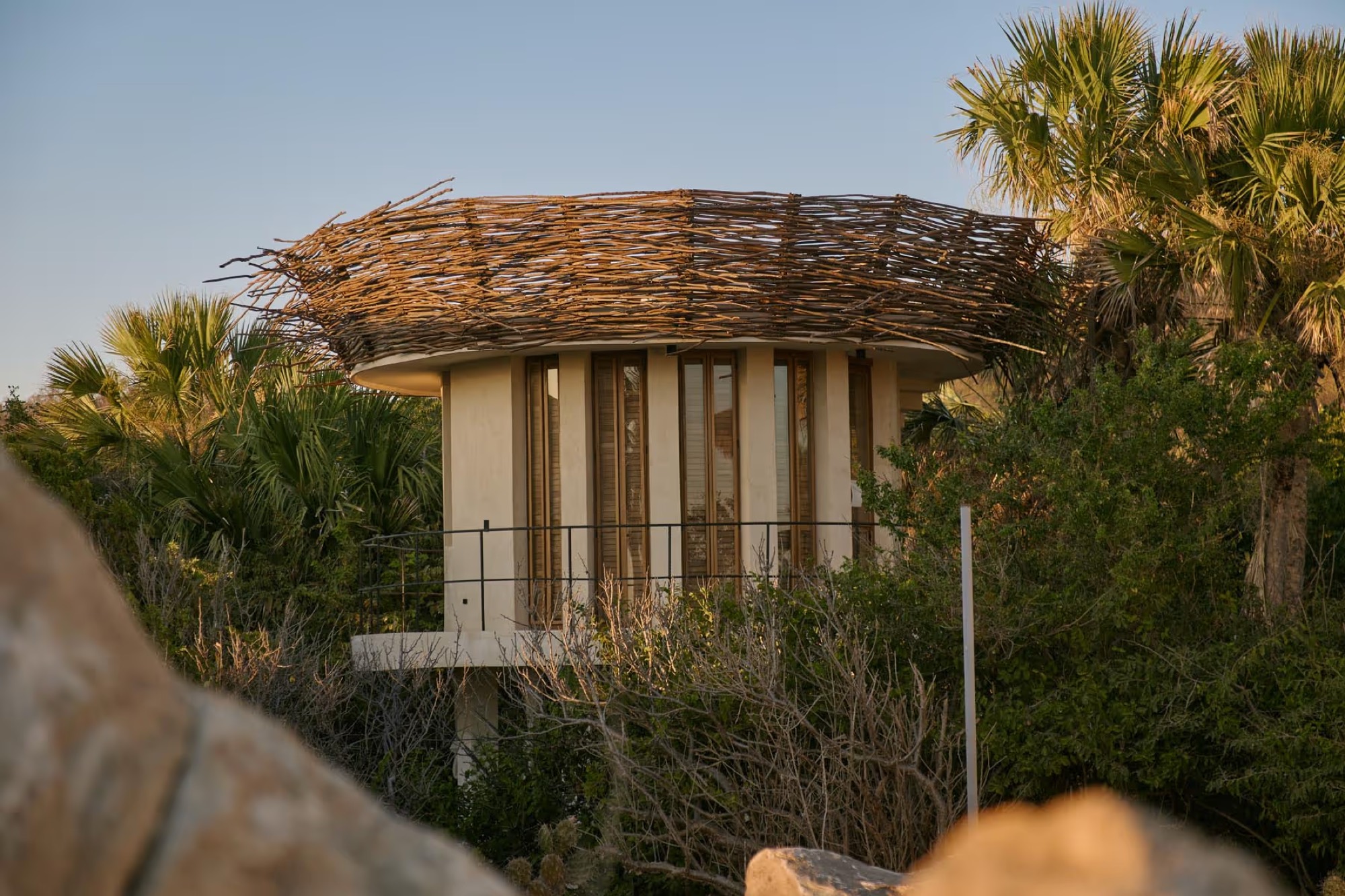 A round villa with a palm-thatch roof among fan palms